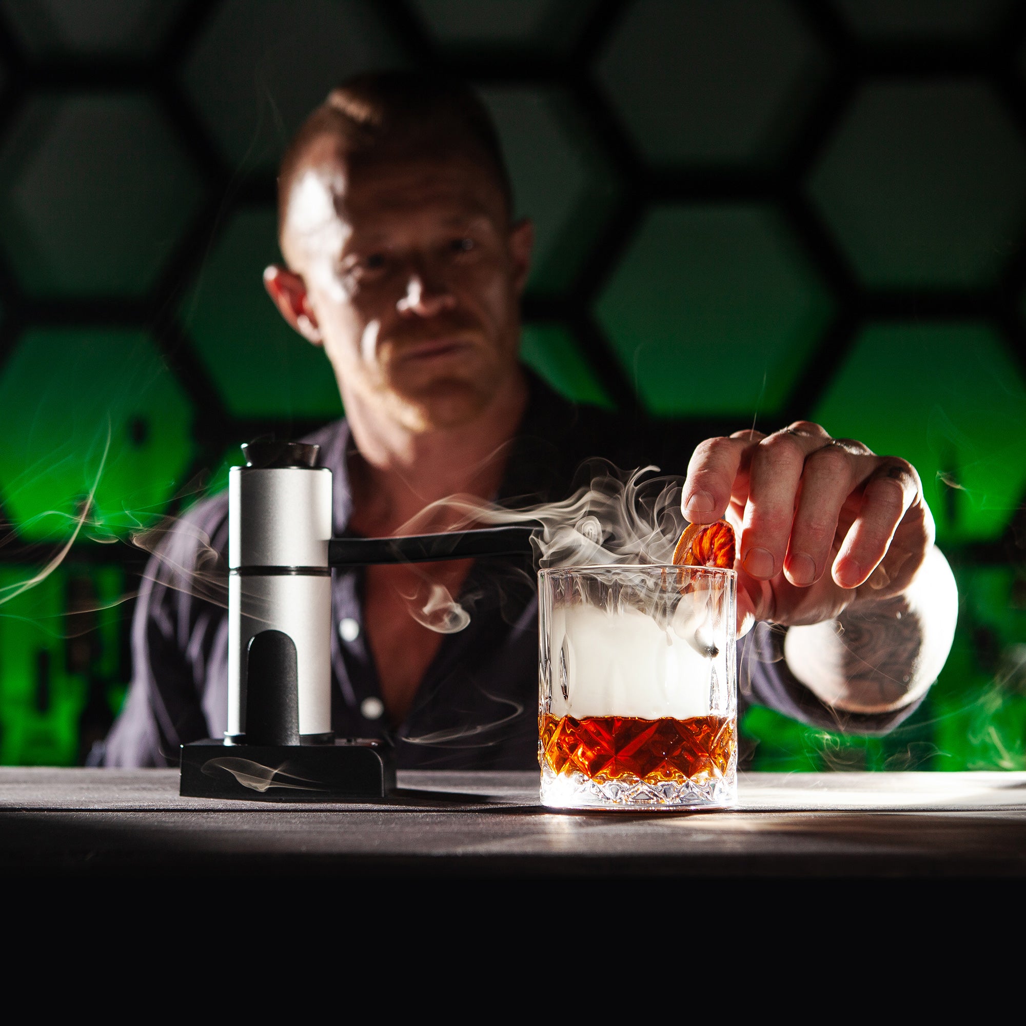 Man adding a garnish to a smoked Negroni cocktail with the Sixpence Alchemy smoke infuser gun in background