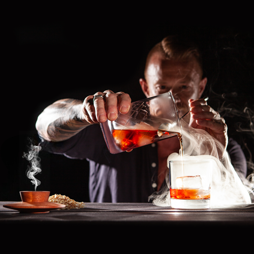 Man pouring a smoked Negroni into a glass while the single hardwood smoker sits on a bar