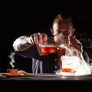 Man pouring a smoked Negroni into a glass while the single hardwood smoker sits on a bar