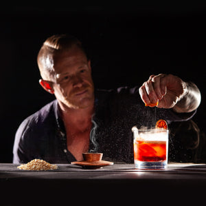 man garnishing a smoked Negroni cocktail with the Sixpence Alchemy hardwood cocktail smoker