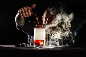 Man lighting the Sixpence Alchemy hardwood smoke top sitting atop a mixing glass filled with a Smoked Negroni Cocktail in an Australian bar