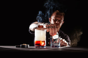 Barman preparing a glass to pour his smoked Negroni after using the Sixpence Alchemy Deluxe hardwood Cocktail Smoker