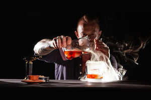 Pouring a smoking Negroni Cocktail from a mixing glass after using the Sixpence Alchemy cocktail smoker with Butane torch and natural flavoured woodchips