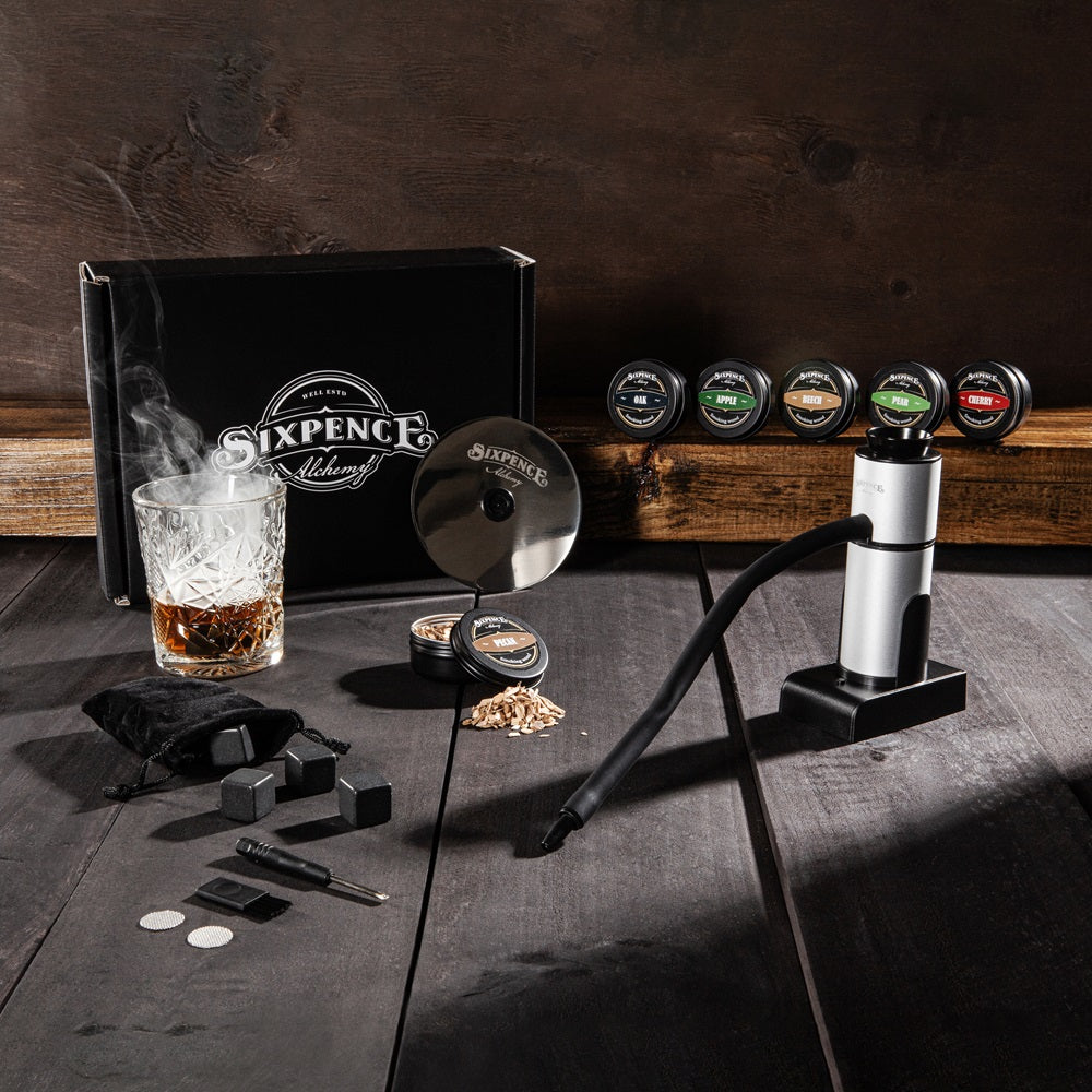 Sixpence Alchemy Food and Drink Smoke Infuser Kit with 6 wood chip tins, whisky rocks and drink cover disc on a dark countertop