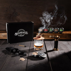 Home Bar Gift Complete Whiskey Smoking Kit with butane torch, 6 natural wood chip tins, hardwood smoke top, granite whiskey rocks, cleaning brush and gift box on a countertop